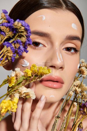 A brunette woman gracefully holds flowers in front of her face, showcasing femininity and natures beauty.