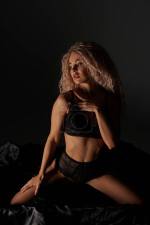 Photo for A seductive woman in lingerie sits provocatively on a bed, exuding confidence and allure. - Royalty Free Image