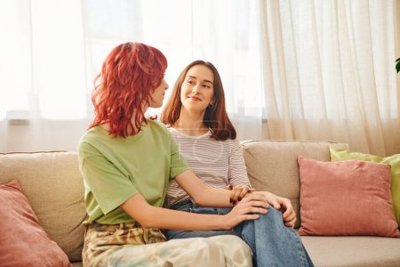 Two young lesbian women sharing a tender moment on a cozy sofa, couple locked in a loving gaze