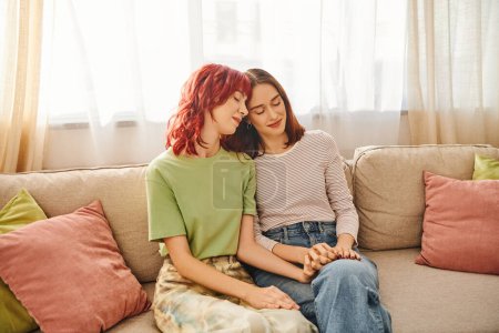 tenderness, young and pleased lgbt couple in casual attire holding hands and sitting on sofa