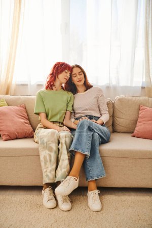 partnership, young and pleased lgbt couple in casual attire holding hands and sitting on sofa