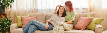 Téléchargez les photos : Jeune couple lesbien dans sa vingtaine profiter du temps ensemble tout en se reposant sur le canapé dans le salon, bannière - en image libre de droit