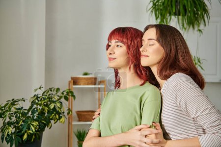 portrait of young lesbian couple embracing while looking away, their faces full of bliss and joy
