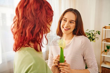 Tender moment of lesbian couple, woman gifting tulip to her happy girlfriend, symbol of spring love