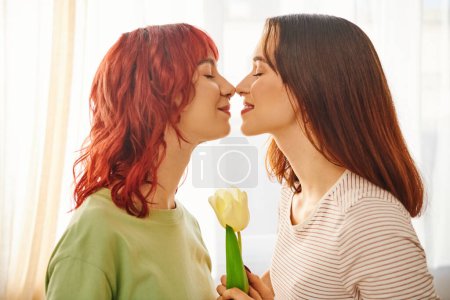Foto de Tender moment of lesbian couple standing nose to nose near blooming tulip, symbol of spring - Imagen libre de derechos