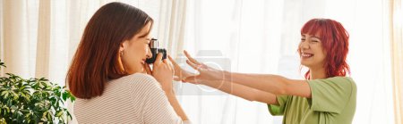 Photo for Home photo session of lesbian woman capturing her girlfriend pose with outstretched hands, banner - Royalty Free Image