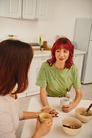 Téléchargez les photos : Cozy moment of a happy young lesbian couple holding hands during breakfast in a cozy kitchen - en image libre de droit