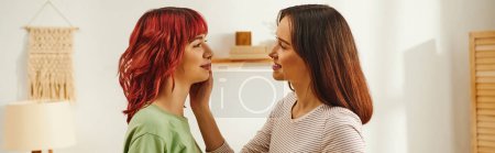 happy young lesbian woman adjusting hair of her cheerful girlfriend in modern apartment, banner