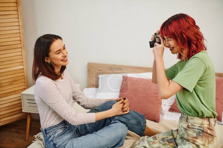 Photo for Candid photo session of happy lesbian woman taking photo on retro camera of her girlfriend on bed - Royalty Free Image