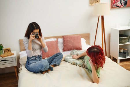 home photo session of lesbian woman taking photo on retro camera of her girlfriend on bed