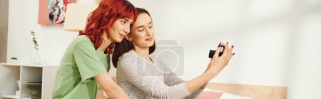 pancarta de sesión de fotos en casa de feliz joven pareja de lesbianas tomando selfie en la cámara retro en el dormitorio