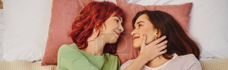 vue du haut du couple lesbien souriant se regardant et couchés ensemble sur le lit, bannière