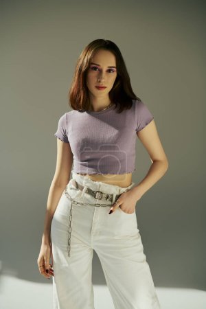 stylish gen z woman in 20s posing in purple t-shirt, standing with hand in pocket of white jeans
