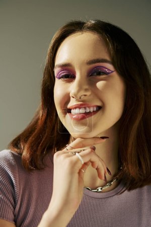 bold makeup of happy gen z girl posing in t-shirt and looking at camera, purple eye shadow