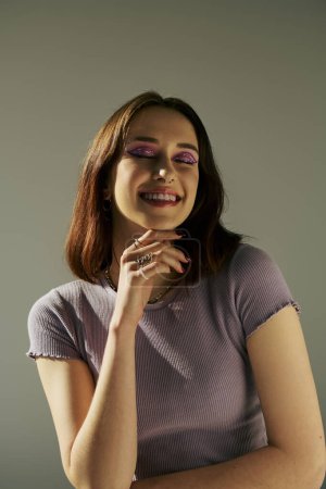 bold makeup of happy young girl in 20s posing in t-shirt with closed eyes and purple eye shadow