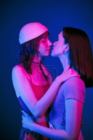 Foto de Beso sensual bajo luces púrpuras de pareja lesbiana con estilo con maquillaje audaz, generación z amor - Imagen libre de derechos