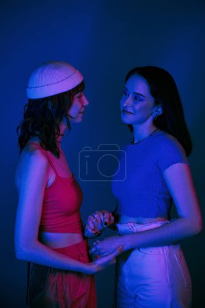 Photo for Happy lgbt couple in 20s, with bold makeup and stylish attire holding hands under purple lights - Royalty Free Image