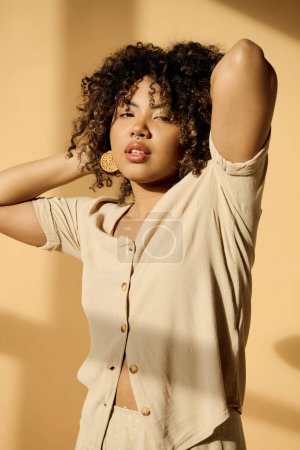 Téléchargez les photos : A beautiful young African American woman with curly hair is stylishly posing for a photo in a studio setting. - en image libre de droit