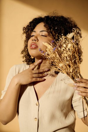 Photo for A beautiful young African American woman with curly hair holding a bunch of dried flowers in a studio setting. - Royalty Free Image