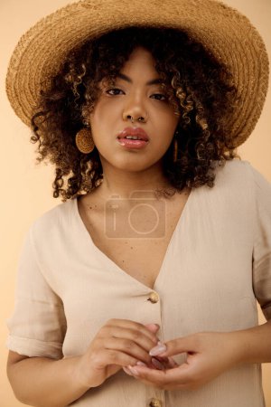 Foto de Una hermosa joven afroamericana con el pelo rizado usando un sombrero de paja y una camisa blanca emana elegancia en un ambiente de estudio. - Imagen libre de derechos