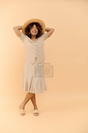 A stylish African American woman with curly hair is confidently posing in a summer dress and hat in a studio setting.