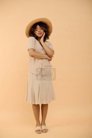Photo for A beautiful young African American woman with curly hair is wearing a hat and a summer dress in a studio setting. - Royalty Free Image