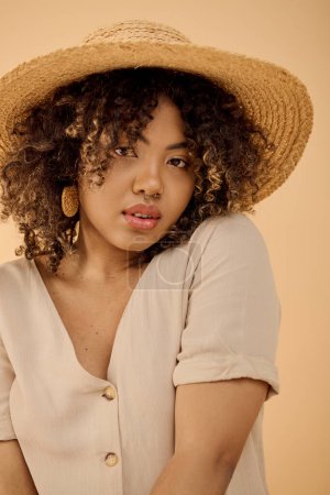 Téléchargez les photos : Une jeune afro-américaine aux cheveux bouclés, coiffée d'un chapeau de paille et d'une chemise blanche, respirant la tranquillité dans un décor de studio. - en image libre de droit