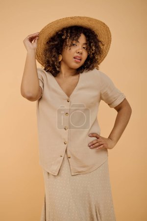 A beautiful young African American woman with curly hair wearing a floral dress and a wide-brimmed hat in a studio setting.