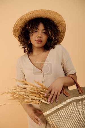 A young African American woman with curly hair in a summer dress holding a bag while wearing a stylish straw hat in a studio setting.