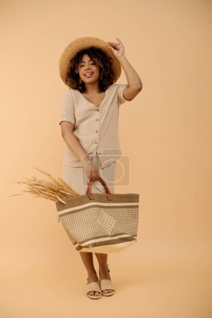 A beautiful young African American woman with curly hair, wearing a hat and dress, holds a basket in a studio setting.