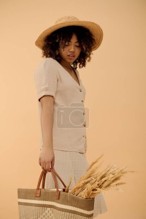 Foto de Una joven afroamericana en un vestido de verano sosteniendo un sombrero de paja y una bolsa, emanando elegancia y estilo. - Imagen libre de derechos