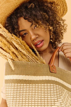 Téléchargez les photos : Une jeune afro-américaine aux cheveux bouclés portant une robe d'été, tenant un sac et portant un élégant chapeau de paille. - en image libre de droit