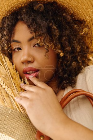 A stylish African American woman in a straw hat holds a brown bag, exuding summer vibes in a studio setting.