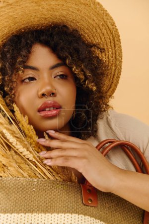Foto de Young African American woman with curly hair in a summer dress, holding a brown bag and wearing a stylish straw hat. - Imagen libre de derechos
