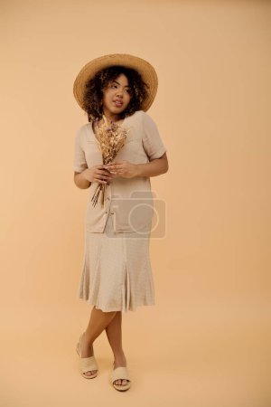 Photo for A beautiful young African American woman with curly hair wearing a straw hat and a summer dress, posing in a studio setting. - Royalty Free Image