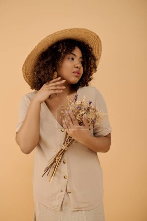 Foto de A young African American woman with curly hair, wearing a hat, holds a bunch of flowers in a studio setting. - Imagen libre de derechos