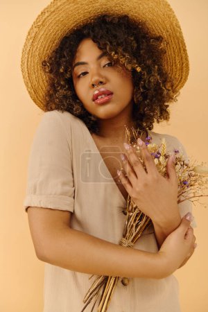 Foto de Una hermosa joven afroamericana con el pelo rizado usando un sombrero de paja, sosteniendo un ramo de flores de colores. - Imagen libre de derechos