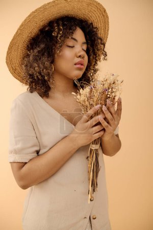 A captivating young African American woman with curly hair, wearing a straw hat, holding a bunch of dried flowers.
