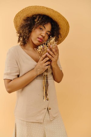 Una mujer afroamericana con estilo se pone un sombrero de paja, agarrando un vibrante ramo de flores con una expresión serena.