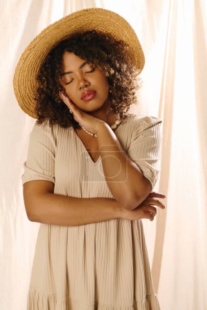 Téléchargez les photos : Une jeune afro-américaine aux cheveux bouclés coiffée d'un chapeau de paille et d'une robe d'été respire la beauté éthéré dans un décor de studio. - en image libre de droit