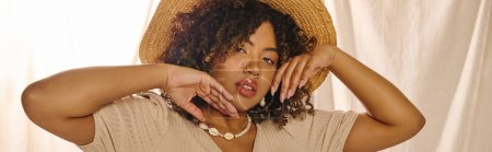 Young African American woman with curly hair in a summer dress, elegant in a straw hat covering her face.