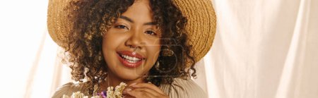 Téléchargez les photos : Une jeune afro-américaine aux cheveux bouclés portant un chapeau de paille, tenant une fleur, exsudant une beauté naturelle dans un décor de studio. - en image libre de droit