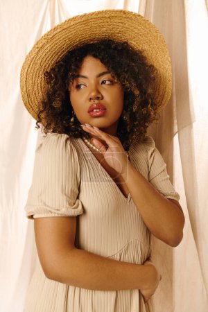 A beautiful young African American woman with curly hair poses gracefully in a studio, wearing a straw hat and a summer dress.
