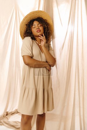 A beautiful young African American woman with curly hair poses for a picture wearing a straw hat in a studio setting.
