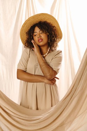 A young African American woman with curly hair in a summer dress, standing gracefully in front of a curtain.