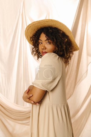 A beautiful young African American woman with curly hair wearing a hat and summer dress in a studio setting.