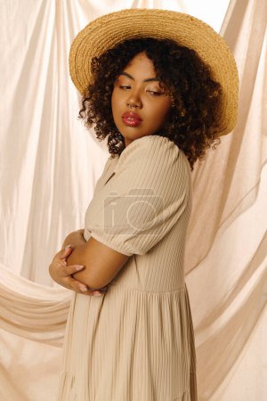 A beautiful young African American woman with curly hair poses in a summer dress and straw hat in a studio setting.