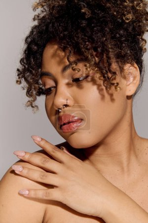 Téléchargez les photos : Une jeune afro-américaine aux cheveux bouclés debout dans un studio, posant doucement sa main sur sa poitrine dans un geste sincère. - en image libre de droit