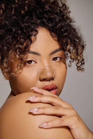 Nahaufnahme einer atemberaubenden jungen Afroamerikanerin mit lockigem Haar in einem Studio-Setting, das Schönheit und Selbstbewusstsein ausstrahlt.