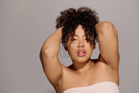Foto de Una hermosa joven afroamericana con el pelo rizado posa graciosamente en un estudio para un retrato. - Imagen libre de derechos